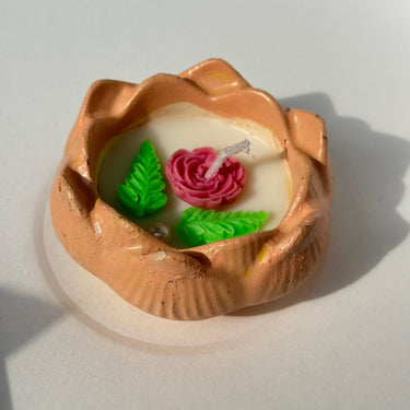 Decorative candle with a rose design in a copper holder on a white background